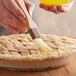 A hand using a Thunder Group Nylon Bristle Pastry Brush with a wooden handle to put pastry on a pie.