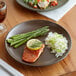 An Acopa Embers hickory brown stoneware plate with rice, asparagus, and salmon on a table.