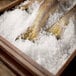 A wooden box filled with ice and fish with a yellow tail sitting on top of ice.
