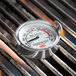 A Cooper-Atkins round dial grill thermometer on a grill.