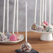 A group of chocolate covered cake pops with white sticks and sprinkles.