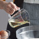 A hand holding a Carlisle clear polycarbonate measuring cup pouring liquid into a bowl of eggs.