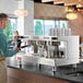 A man standing at a counter with an Estella Caffe three group automatic espresso machine.