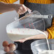 A woman pouring milk into a Carlisle clear measuring cup.