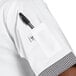 A person wearing a white Uncommon Chef v-neck cook shirt with Shepherd's check trim and a pen in the pocket.