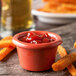 A Carlisle sunset orange melamine ramekin filled with ketchup on a table with sweet potato fries.