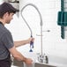 A man in a black shirt and hat holding a Waterloo pre-rinse hose spring over a sink.
