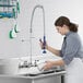 A woman using a Waterloo pre-rinse spray valve to wash dishes in a sink.