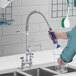 A person using a Waterloo low profile deck-mounted pre-rinse faucet to fill a glass container on a counter in a professional kitchen.