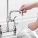 A person's hand pouring water from a Waterloo pre-rinse add-on faucet over a sink.