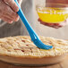 A person using a blue Ateco round silicone pastry brush to decorate a pie.