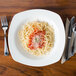 A table set with a CAC Ivory square pasta bowl filled with spaghetti and sauce with a fork.