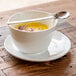 A white Front of the House Harmony cup of soup with a spoon on a saucer.