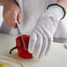 A person wearing MercerGuard white gloves cutting a red pepper on a counter.
