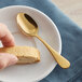 A hand holding a plate with a cookie and a Acopa Vernon Gold stainless steel demitasse spoon.
