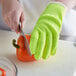 A person wearing yellow Mercer Culinary cut-resistant gloves cutting a red bell pepper on a counter.
