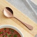 A Vernon Rose Gold stainless steel bouillon spoon with soup in a bowl.