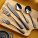 Acopa Vernon black stainless steel flatware on a wooden cutting board.