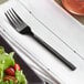 A Acopa Phoenix stainless steel salad fork on a napkin next to a plate of salad.