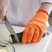 A person in a Mercer Culinary orange glove cutting a zucchini.