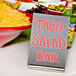 An American Metalcraft stainless steel table card holder with a sign that says "Taco Salad Bar" on a table with a bowl of cheese.