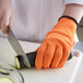 A person wearing an orange Mercer Culinary Millennia cut-resistant glove cutting a zucchini.