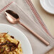 A plate of food with an Acopa Phoenix rose gold stainless steel spoon on the table.