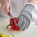 A person wearing a MercerMax Level Cut-Resistant Glove cutting a red pepper.