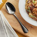 An Acopa Vernon stainless steel oval bowl spoon with a plate of food on a wooden board.
