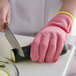 A person wearing a pink Mercer Culinary cut-resistant glove cutting a zucchini with a knife.