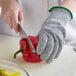 A person wearing MercerMax Level Cut-Resistant gloves cutting a red pepper.
