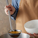 A person using a Vollrath stainless steel ladle to pour liquid into a bowl.