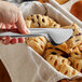 A hand using Vollrath stainless steel pastry tongs to grab a cookie from a basket.