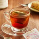 A glass cup of Bigelow Peppermint Bark tea with a tea bag on a saucer.