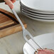 A Vollrath stainless steel serving fork holding a piece of meat on a plate.