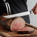 A person cutting a piece of meat with a Vollrath stainless steel carving knife.