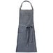 A grey denim Mercer Culinary bib apron with brown leather straps and a tie.