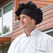A man wearing a black Uncommon Chef poplin chef hat standing in a professional kitchen.