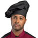 A man wearing a black Uncommon Chef poplin chef hat with black and maroon accents.