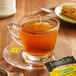 A glass cup of Bigelow Lemon Lift decaffeinated tea with a tea bag on a saucer.