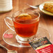 A glass cup of Bigelow Spiced Chai tea on a saucer with a tea bag.