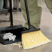 A person using a Carlisle Duo Sweep broom with flagged bristles and a 48" handle to sweep a floor.