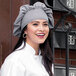 A woman wearing a Uncommon Chef Houndstooth twill chef hat with a smile.