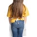 A little girl with long hair wearing a white Uncommon Chef bib apron over a yellow shirt and blue jeans.