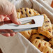 A person's hand using Vollrath stainless steel tongs to pick up a pastry.