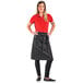 A woman wearing a Mercer Culinary black denim bistro apron with black leather details.