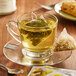 A glass cup of Steep Cafe green tea with a tea bag on a saucer.