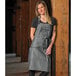 A woman wearing a Mercer Culinary black denim bib apron with leather accents.