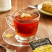 A glass cup of Bigelow Vanilla Caramel tea with a tea bag on a saucer.