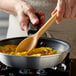 A person using a Vollrath tan high heat nylon prep spoon to stir food in a pan.